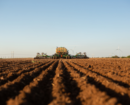 Photo shows a tractor and seeding implement in the distance with new furrows where wheat was planted in the foreground to suggest prospective plantings.