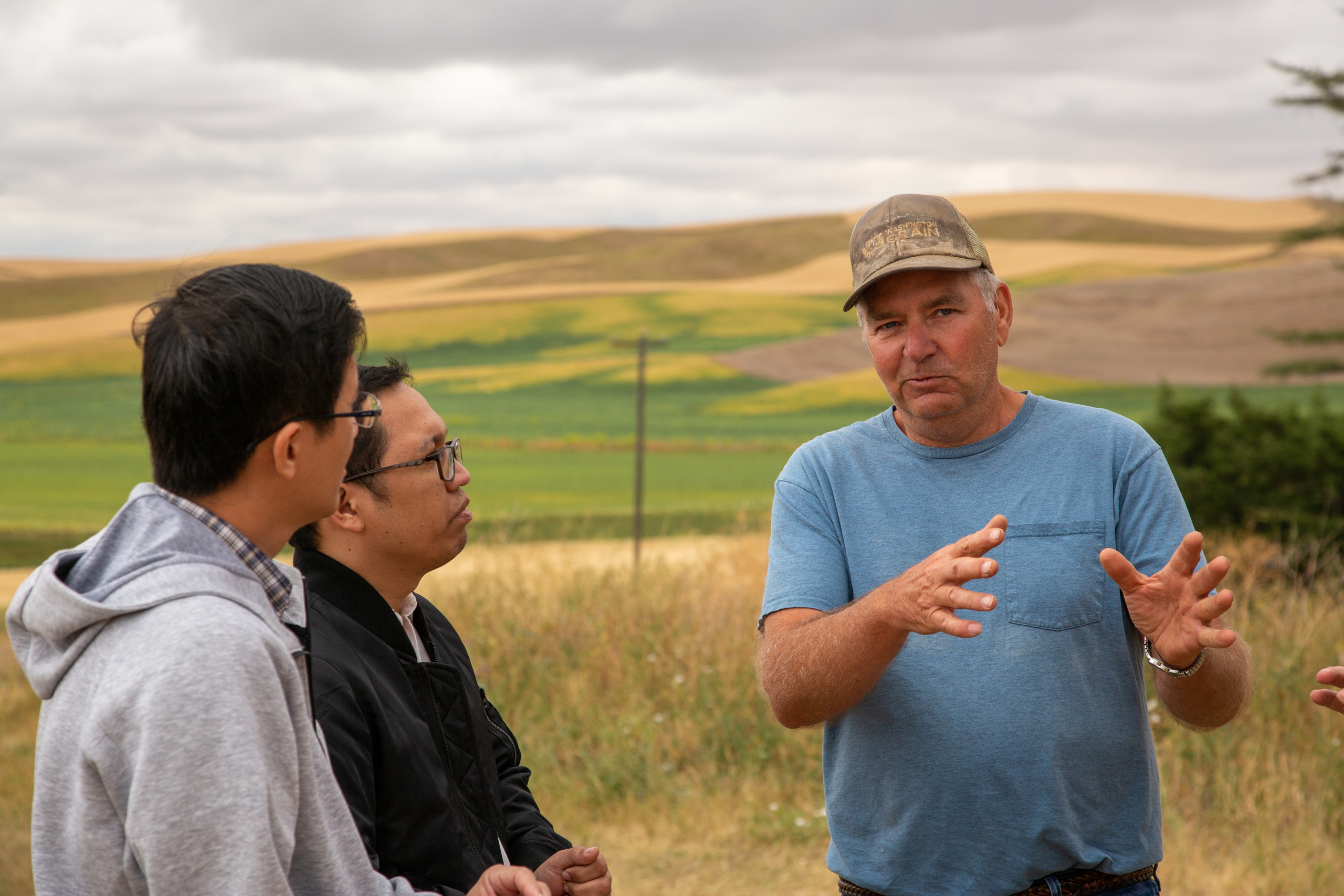 Photo of Washington wheat farmer Gary Bailey talking with wheat buyers from Myanmar and Malaysia on his farm in 2020 with wheat fields in the hills behind them, illustrating one of the Stories of Stewardship.