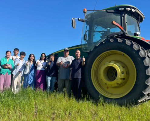 Photo shows people from USW, Oregon Wheat Commission, farmer, and a team of Chinese bakers at a farm in Oregon by a tractor giving thumbs up.