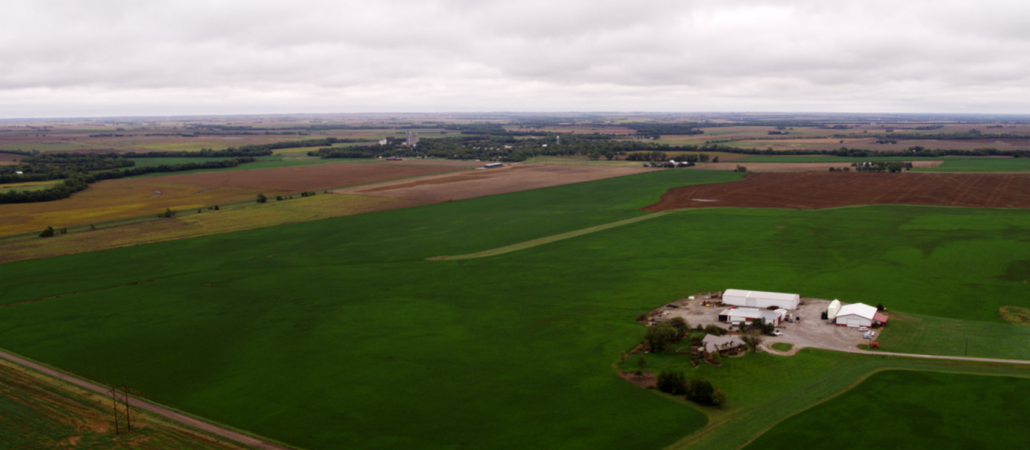 Panaramic image of the Knopf family farm in central Kansas including a farm stead, green fields and ripe wheat field in the background on a cloudy day.