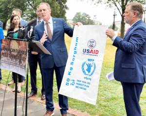 Rep. Tracey Mann (R-KS) addresses the media while holding a U.S. Food Aid sack with and Rep. Rick Crawford (R-AR) during a press conference announcing the introduction of the American Farmers Feed the World Act 2023.