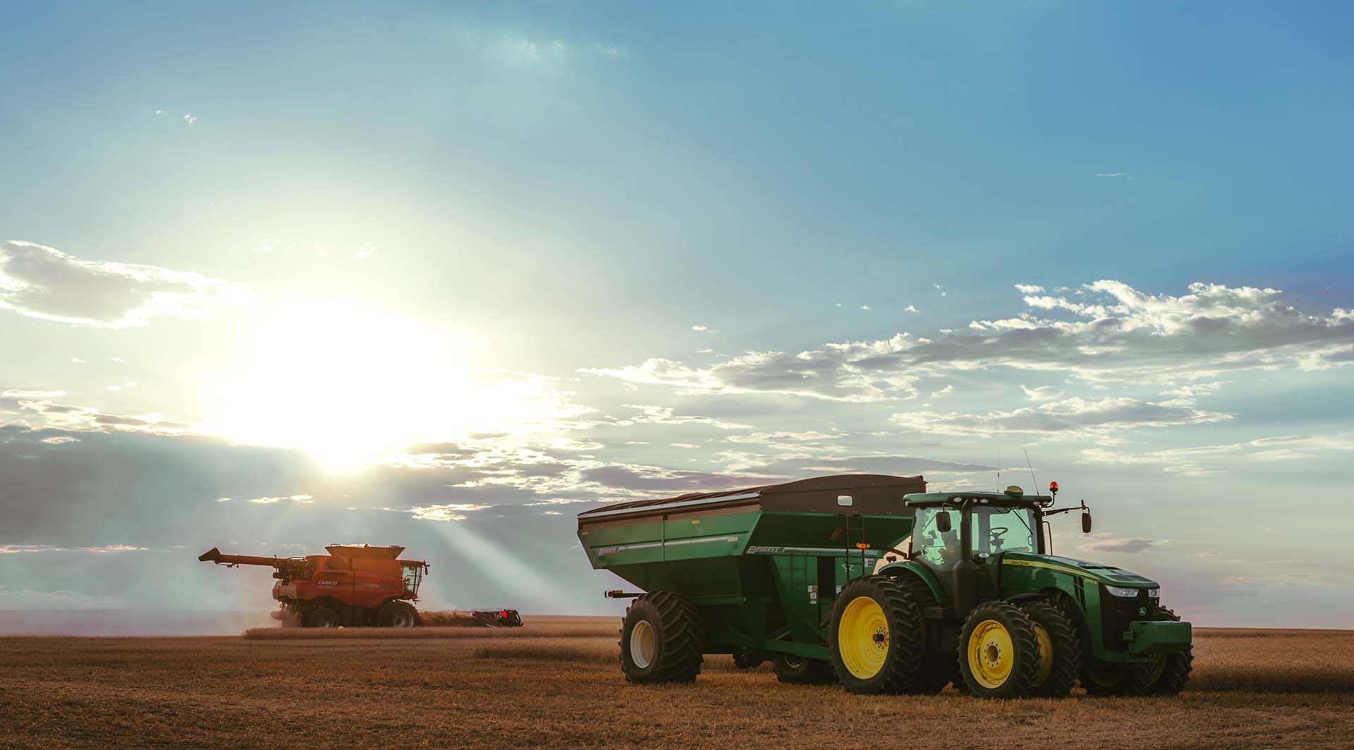Near sunset, a red combine harvests wheat while a tractor and grain cart wait to get a load in Nebraska.