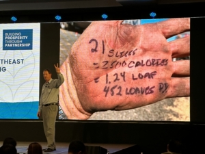 Darren Padget stands in front of a panel with a photo of his hand with his calculation of how much bread can be made from wheat grown on his farm at the South And Southeast Asian Marketing Conference.