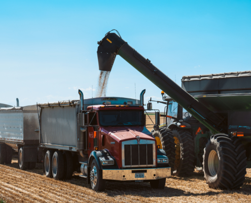 Photo of a combine unloading wheat into a semi-trailer.